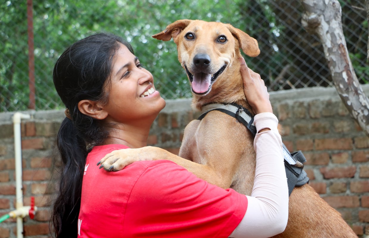 Indian woman laughs and cuddles dog who has jumped into her arms